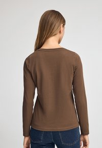 Brun långärmad skjorta med rund halsringning, gjord av mjukt tyg. Enkelt mönster med rena sömmar, kombinerad med denimjeans.