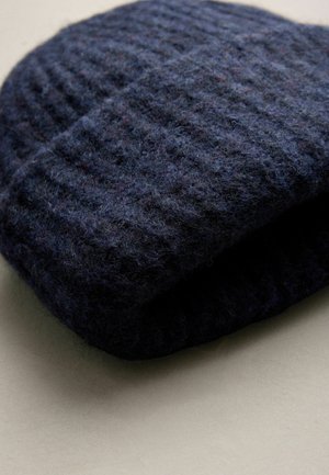 Tumesinine ribatud kudum beanie, mis on valmistatud pehmest villast, millel on tekstuuriga muster ja pehme viimistlus, volditud ääres, et pakkuda mugavat istuvust.