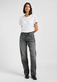 Camiseta blanca de manga corta combinada con unos pantalones vaqueros de talle alto en negro desgastado. Los pantalones presentan costuras destacadas y un diseño clásico de cinco bolsillos.