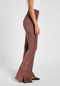 Pantaloni a palazzo in corduroy di colore rosa tenue con righe verticali, vita alta e spacchi laterali all'orlo, abbinati a scarpe nere a punta.