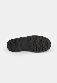 Suela de bota de goma negra con un patrón de relieve texturizado, que presenta formas hexagonales prominentes y surcos profundos para tracción.