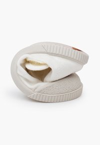 Witte canvas schoen met een gestructureerde grijze rubberen zool, opgerold tot een compacte vorm. Zachte binnenvoering, eenvoudig ontwerp zonder patronen.