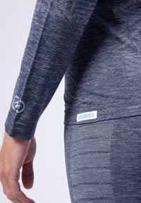 Sportieve lange mouwen shirt in donkergrijs met een gestructureerd patroon, met een logo op de mouw en een blauw label aan de onderrand.