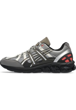 Zapatilla deportiva gris con parte superior de malla, acentos plateados reflectantes, suela negra y tela texturizada. Presenta un sistema de cordones flexible y un cuello acolchado.