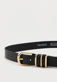 Svart lærbelte med gullmetallspenne, som har tre dekorative utskjæringer nær spennen og jevnt fordelte hull gjennom hele.