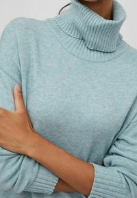 Turkos stickad tröja med ribbad hög hals och uppvikt ärm, med en mjuk textur och avslappnad passform.