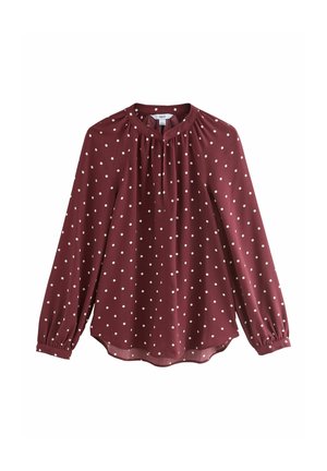 Blouse bordeaux à manches longues avec des pois blancs, col froncé et poignets boutonnés.