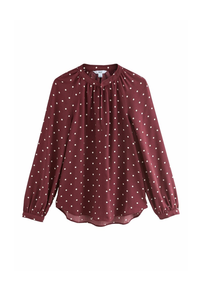 Blouse bordeaux à manches longues avec des pois blancs, col froncé et poignets boutonnés.