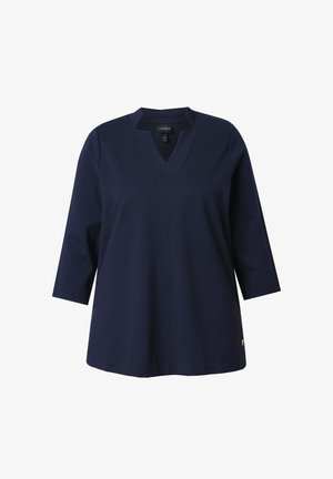 Tmavě modrý top s výstřihem do V a tříčtvrtečními rukávy, vyrobený z hladké látky; má malý emblém na spodní straně.