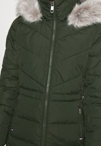 Zielona kurtka puchowa z kołnierzem wykończonym sztucznym futrem, z zamkiem błyskawicznym z przodu, ukośnymi przeszyciami i bocznymi kieszeniami.