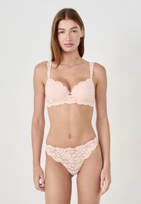 Set di lingerie in pizzo rosa che presenta un reggiseno imbottito con motivo floreale e bordi ondulati, abbinato a un perizoma in pizzo coordinato con dettagli simili.