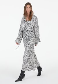 Langes, fließendes Kleid und Blusenset in Schwarz-Weiß-Schlangenprint. Mit langen Ärmeln, einem Tie-Bindegürtel in der Taille und einer weichen Textur. Kombiniert mit schwarzen Stiefeletten.