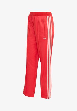 Crvene sportske hlače od glatkog materijala, s uskim strukom, džepom na patentni zatvarač i trima bijelim bočnim prugama s malim logotipom.
