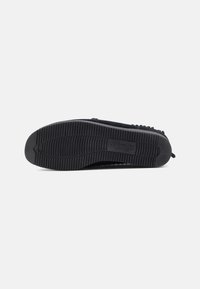 Sapatos pretos com uma sola de borracha texturizada, apresentando sulcos horizontais e uma superfície inferior lisa. Sem marcas ou embelezamentos visíveis.