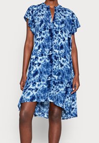 Modrý tie-dye šaty s výstřihem do V, krátkými volánovými rukávy a lemem ve vysoké a nízké části. Látka je lehká s texturovaným vzhledem.