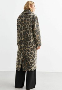 Beige en zwarte wollen lange jas met luipaardprint, voorzien van een brede kraag, zij-splitten en een oversized pasvorm, gecombineerd met zwarte broek.
