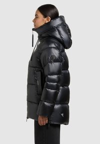 Chaqueta negra acolchada con acabado brillante, capucha grande, bolsillos con cremallera y detalles elásticos. Presenta un diseño acolchado para aislamiento.