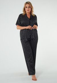 Czarny komplet piżamowy składający się z krótkiego rękawa i długich spodni ozdobiony małymi białymi sercami. Gładka tekstura z kontrastującymi białymi detalami krawędzi.