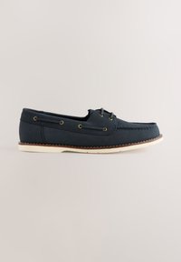 Chaussure bateau en cuir bleu marine avec semelle blanche, coutures moc toe et détails de lacets sur les côtés et le dessus, présentée de profil sur fond neutre.
