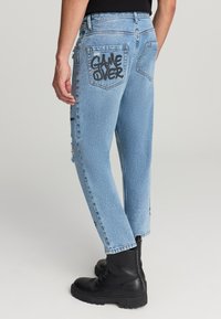 Jeans in denim azzurro chiaro con accenti strappati, caratterizzati da una grafica 'GAME OVER' sui taschini posteriori e un design a gamba dritta.