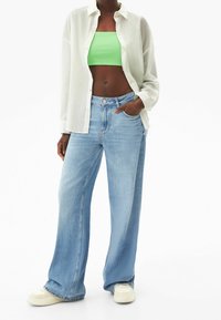 Wide-leg blue denim jeans paired with a green cropped top and a white button-up shirt. Features a relaxed fit and front pocket.