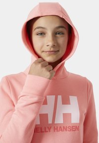 Sudadera rosa claro con un bolsillo canguro en la parte frontal y un logo blanco "HH". Cuenta con puños acanalados y una capucha con cordón. Textura suave.