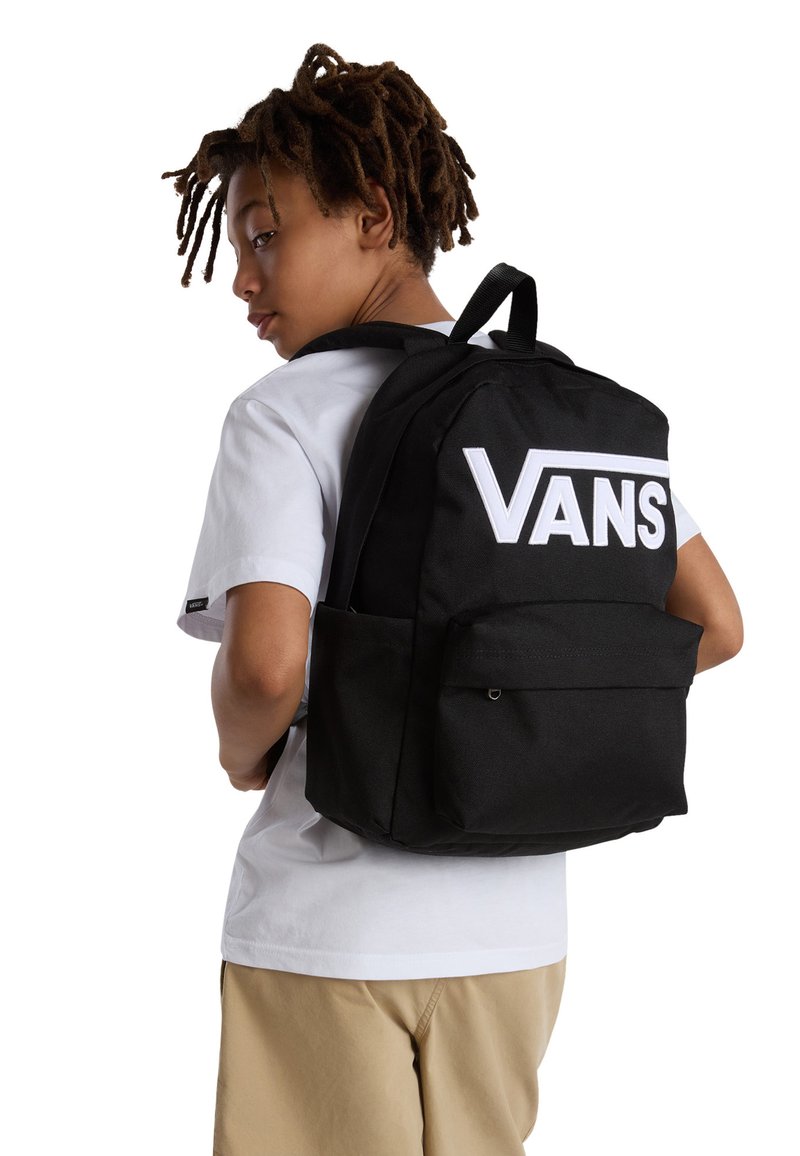 Černý látkový batoh s velkým bílým logem "VANS", přední kapsou a nastavitelými popruhy. Nese ho dítě v bílém tričku.