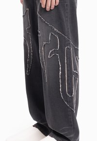 Czarne dżinsy z denimu z postrzępionymi detalami i dużymi wzorami graficznymi. Luźny krój z przetartą fakturą, podkreślający nowoczesny design.