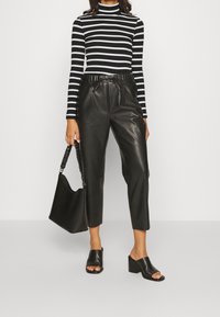 Zwart-wit gestreepte coltrui, zwarte leren cropped broek, open teen zwarte block-heeled mules en een zwarte schoudertas.