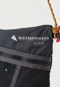 Μαύρη τσάντα από νάιλον με διακοσμητικά από διχτυωτό ύφασμα, έντονο λογότυπο και κλείσιμο με φερμουάρ. Διαθέτει πολύχρωμο κορδόνι ως χερούλι και τριγωνική λεπτομέρεια με το λογότυπο.