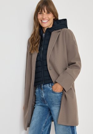 Brun ullkappa med skräddarsydd design, oversized passform och enstaka knappstängning, lager-på-lager över en marinblå puffjacka. Blå denimjeans.