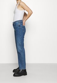 Jeans de denim azul con un corte relajado, cintura alta y sutiles bolsillos traseros, combinados con botas de plataforma negras y una camiseta sin mangas blanca.