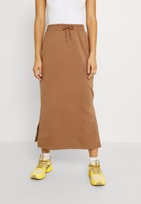 Un haut sans manches blanc associé à une jupe midi brune avec taille à cordon et fente latérale, porté avec des baskets jaunes et des chaussettes blanches.