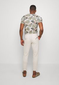 Kortärmad skjorta med ett grönt och blommigt mönster, i kombination med ljusbeige byxor och bruna slip-on skor. Bakifrån.