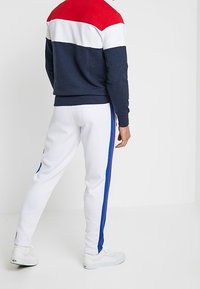 Mikina s červenými, bílými a námořnickými barevnými bloky; žebrované manžety. Bílé joggery s modrými bočními pruhy; hladká tkanina, elastický pas.