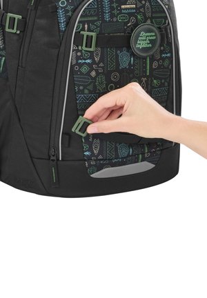 Main ajustant une boucle verte sur un sac à dos noir avec des motifs bleus et verts et un patch rond portant l'inscription « Les rêves grandiront ensemble. »