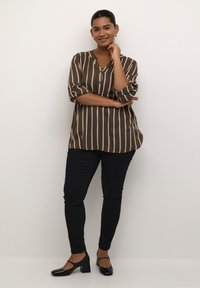Brown and cream striped blouse with a V-neck and button placket, paired with black skinny jeans and black block-heeled shoes.