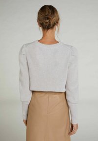 Ljusgrå stickad tröja med puffärmar, ribbad struktur och rundad halsringning, kombinerad med en stilren beige lädernederdel.