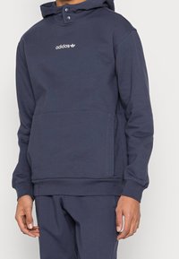 Mörkblå Adidas hoodie med framficka och huva med tryckknapp, matchad med mörkblå sweatpants.