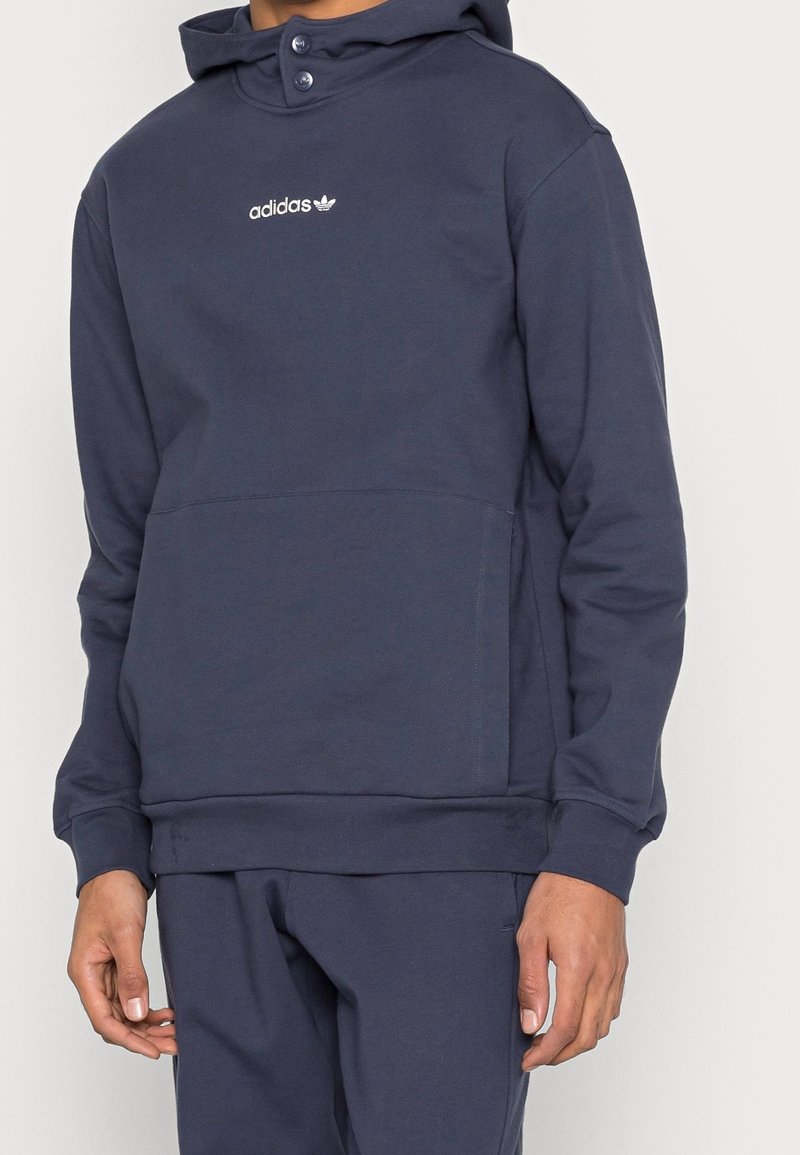 Mörkblå Adidas hoodie med framficka och huva med tryckknapp, matchad med mörkblå sweatpants.