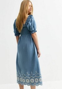 Vestido de algodón azul con mangas abullonadas y cuerpo fruncido. Presenta bordados florales blancos a lo largo del dobladillo. Silueta de longitud media.