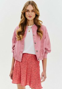 Różowa dżinsowa kurtka bomberka z kwiatowymi wycięciami, w połączeniu z białą koszulką i różową spódnicą w kwiaty, z falbanistym krojem.