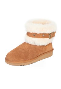 Beige Wildleder-Stiefeletten mit einem weichen weißen Kunstfellbund, akzentuiert durch einen braunen Riemen mit metallischen Nieten und einer Schnalle. Flache Gummisohle.