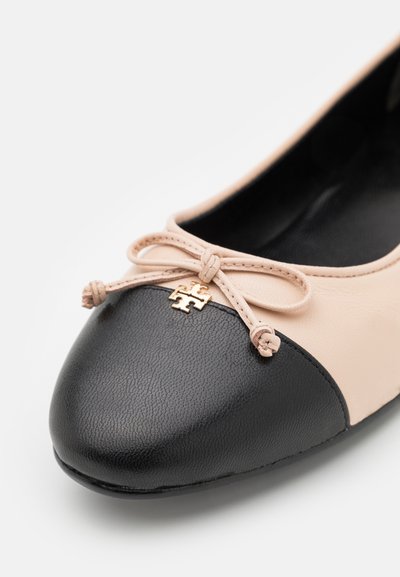 Ballerines en cuir beige avec un capuchon noir texturé, un nœud décoratif et des accents dorés. Doublure intérieure lisse.
