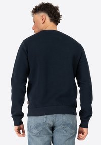Navy blue cotton sweatshirt with long sleeves, ribbed cuffs, and waistband. Features a subtle logo patch on the lower side.