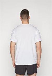 Camiseta blanca de manga corta, cuello redondo, material texturizado, combinada con pantalones cortos oscuros, vista desde la parte posterior sobre un fondo liso.