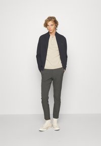 Mornarska pletena bomber jakna, bež polo majica, sivo karirane hlače i off-white visoke tenisice. Glatka tekstura, prilagođeni kroj, jednostavan dizajn.