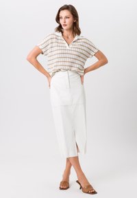 Korte mouw, ivoorkleurig gestreept brei-top met een kraag, gecombineerd met een wit hooggesneden kokerrok met een split aan de voorkant. Bruine sandalen.