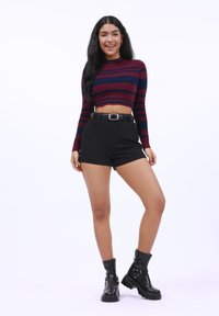 Red and navy striped cropped sweater, black high-waisted shorts with belt, and black ankle boots with buckle detail.