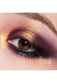 Close-up of an eye with purple and gold eyeshadow, highlighting a metallic sheen, dark eyeliner, and a warm brown iris.